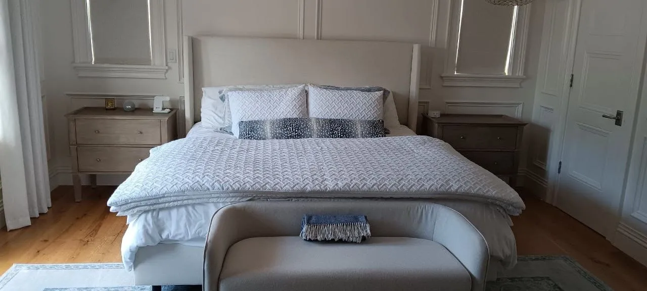 A made bed with white linens and a navy pillow in a bright bedroom