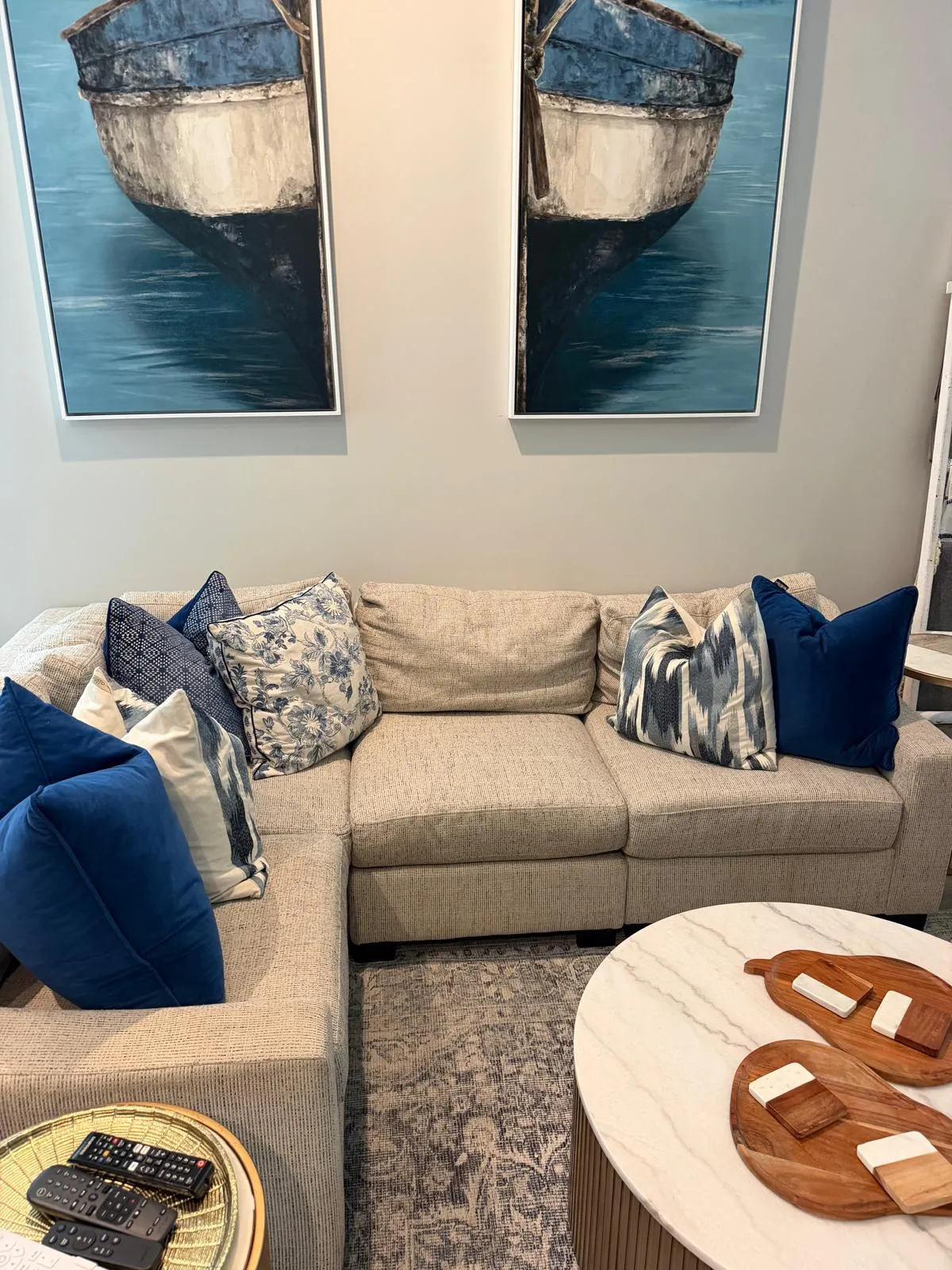 A bright living room with a beige sectional, navy pillows and two framed boat paintings