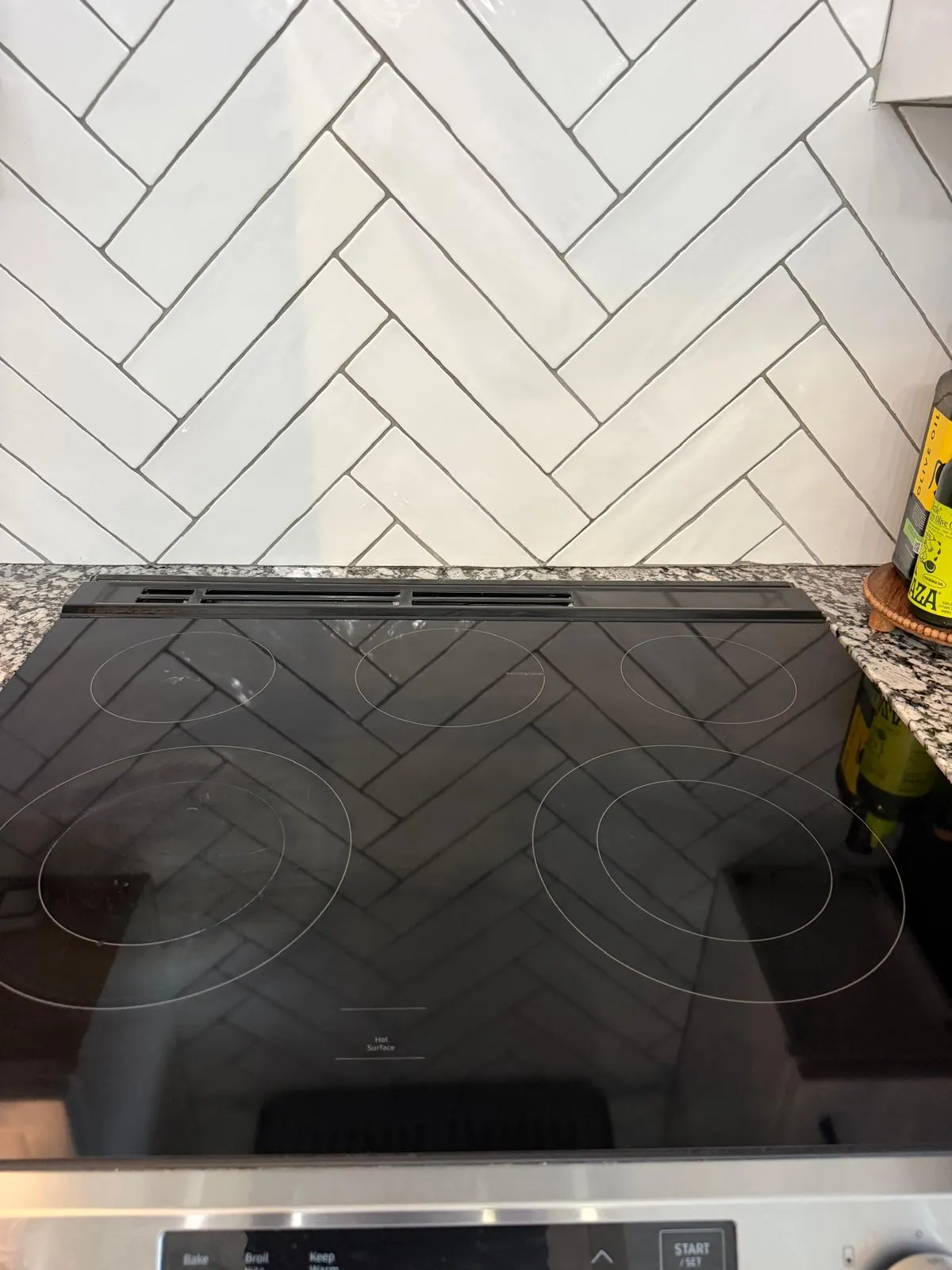 A clean black glass cooktop against a white herringbone tile backsplash
