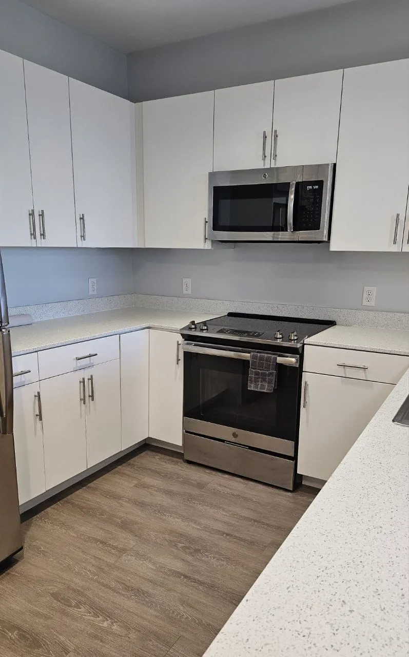 An empty kitchen with white cabinets, stainless steel appliances and clean floors