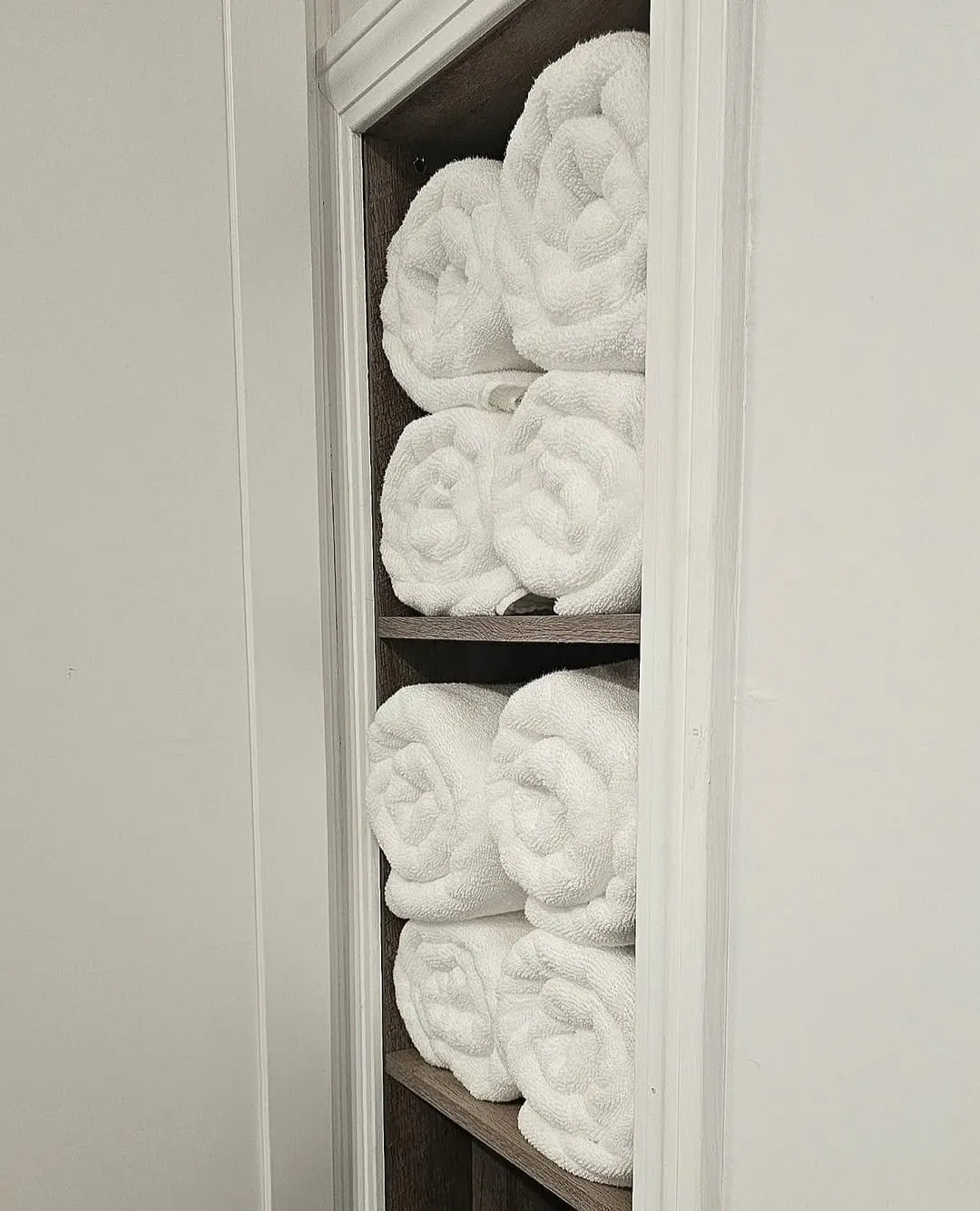 White towels rolled and stacked on a bathroom shelf