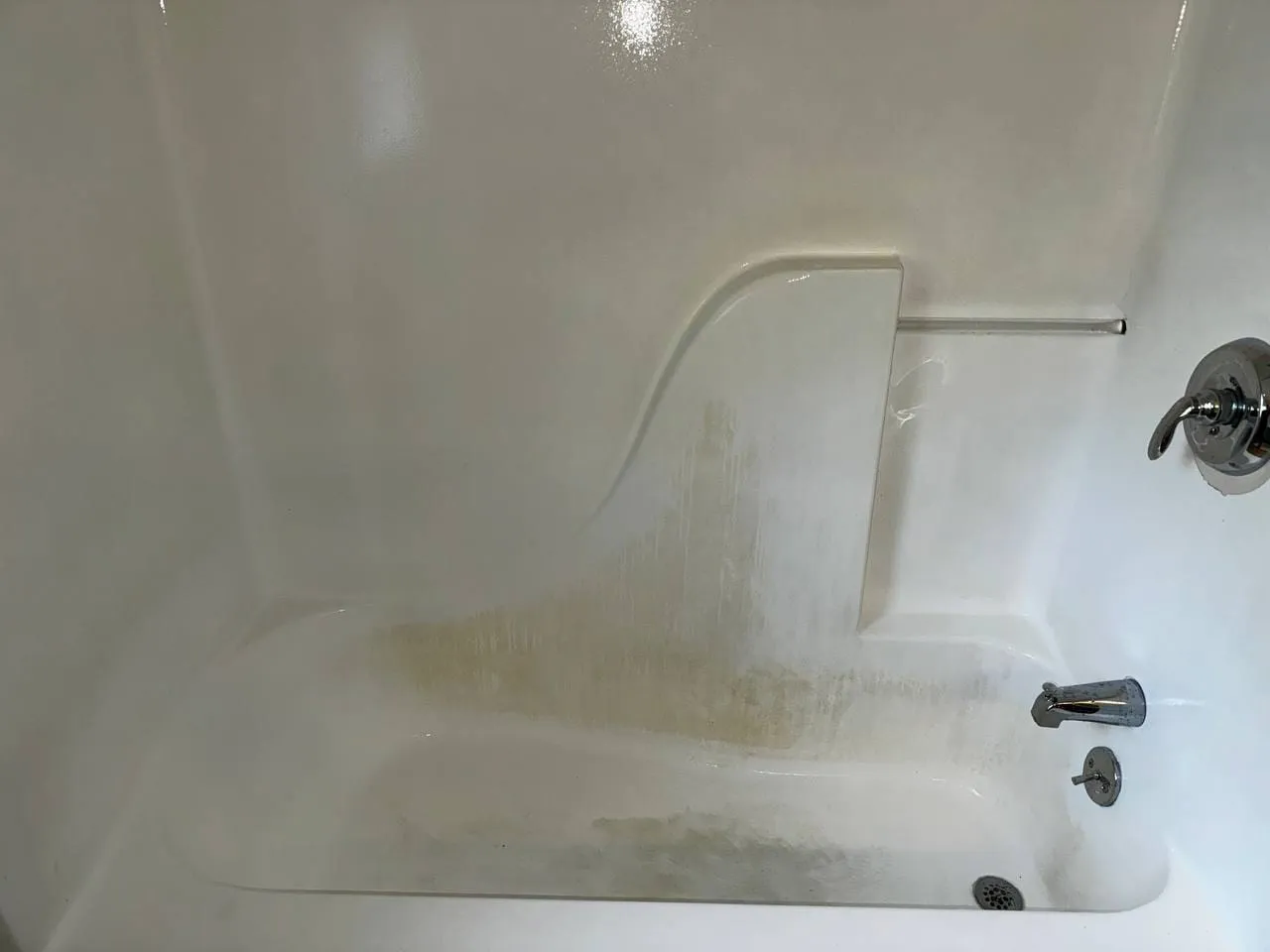 A shower and tub with yellow stains along the bottom, before cleaning